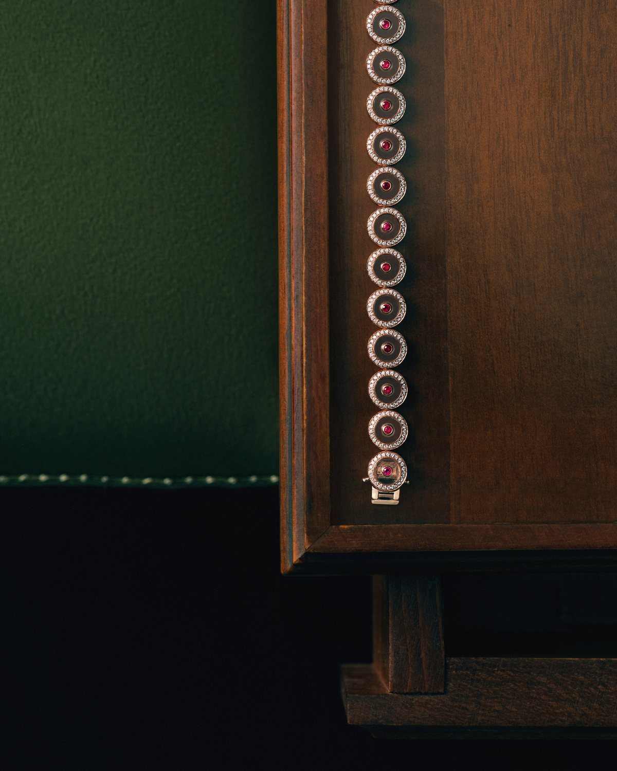 Ruby Circle Tennis Bracelet laid along an antique wooden cabinet