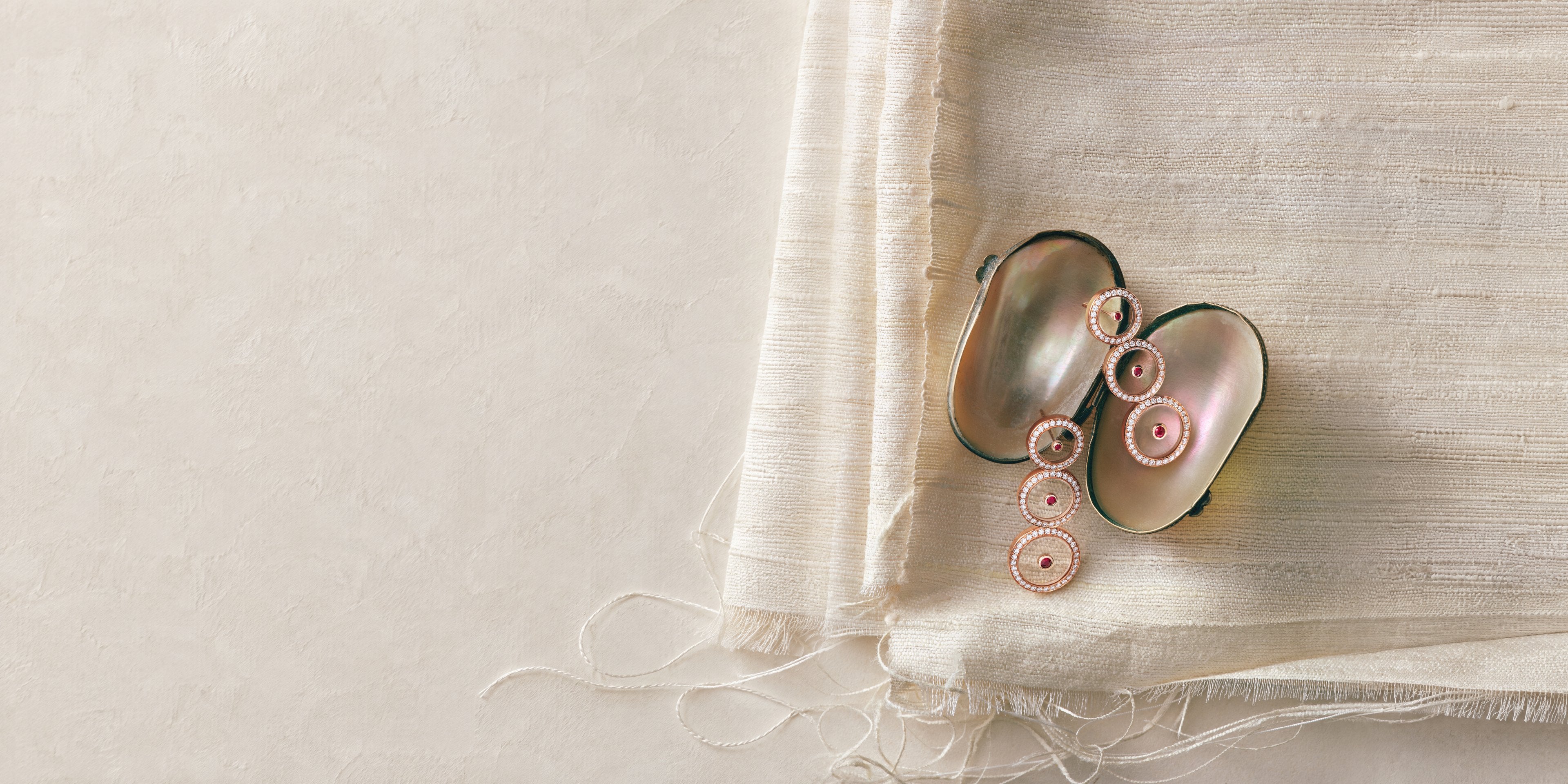 Ruby Graduated Circle Drop Earrings in 18K rose gold on an open mother-of-pearl shell, over folds of ivory raw silk