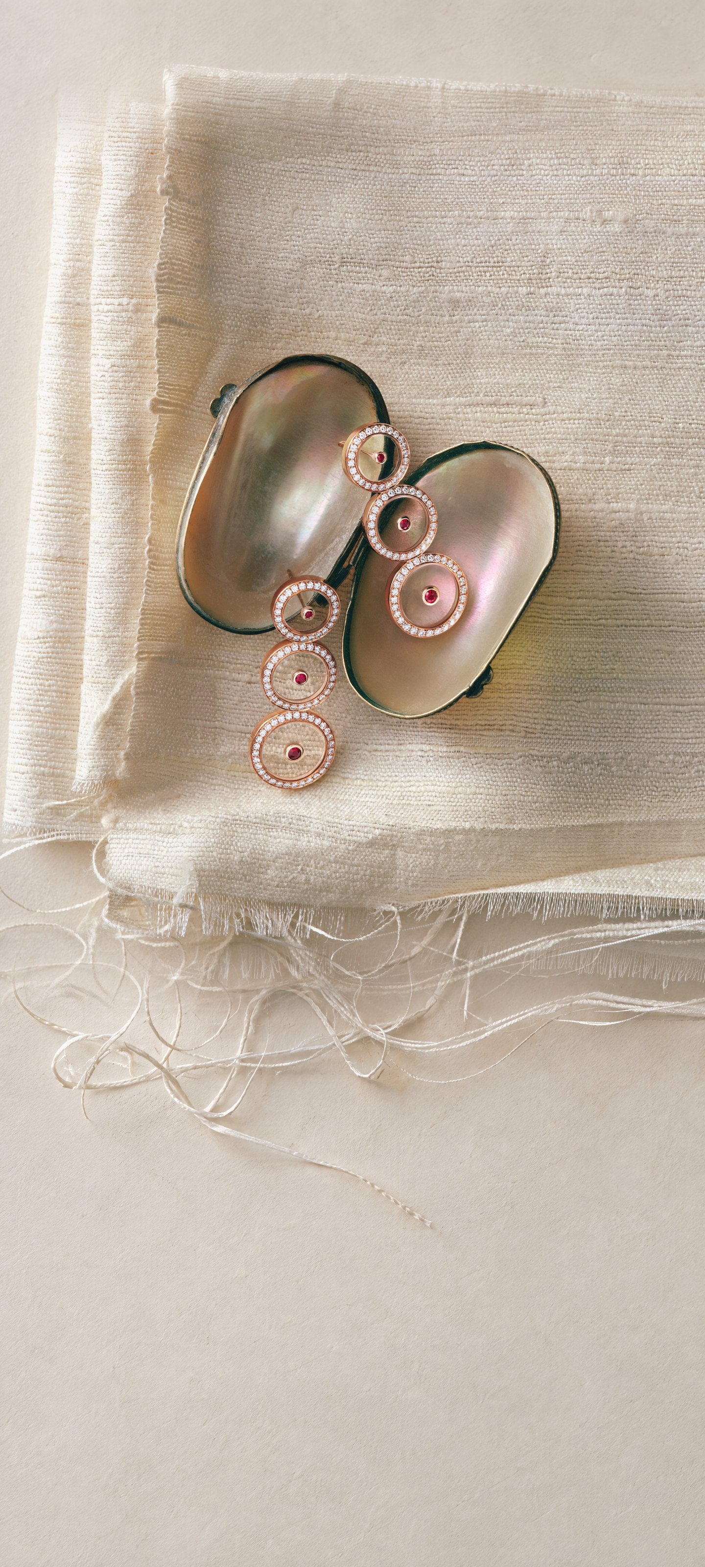 Ruby Graduated Circle Drop Earrings in 18K rose gold on an open mother-of-pearl shell, over folds of ivory raw silk